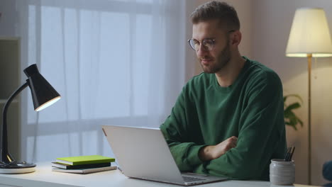 online-communication-by-video-chat-young-man-dressed-green-sweatshirt-and-glasses-is-looking-at-display-of-notebook-and-nodding-head-portrait-shot-in-living-room
